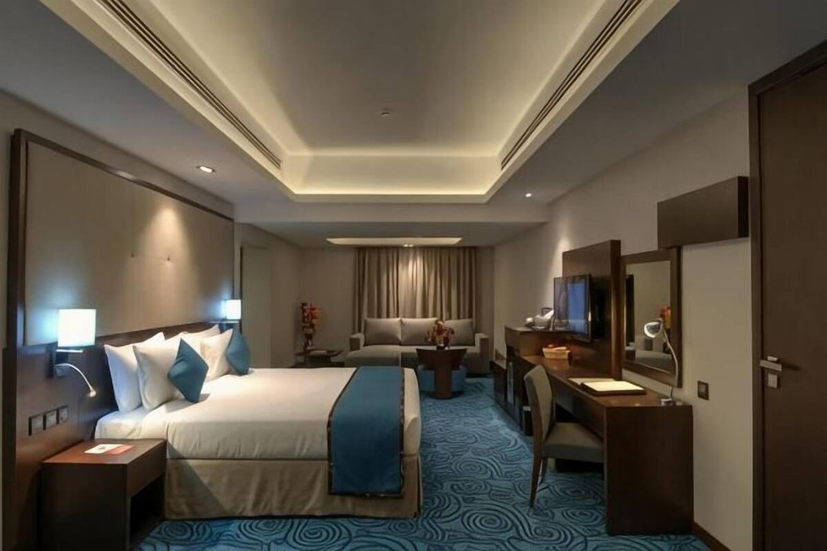 A hotel room with a bed, desk, chair, and a large mirror.
