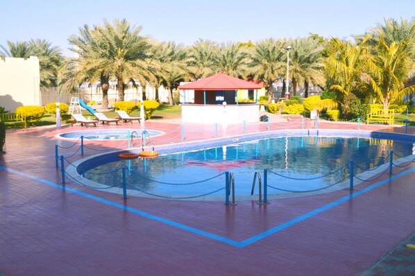 Una piscina con un pabellón de techo rojo, rodeada de palmeras y tumbonas.