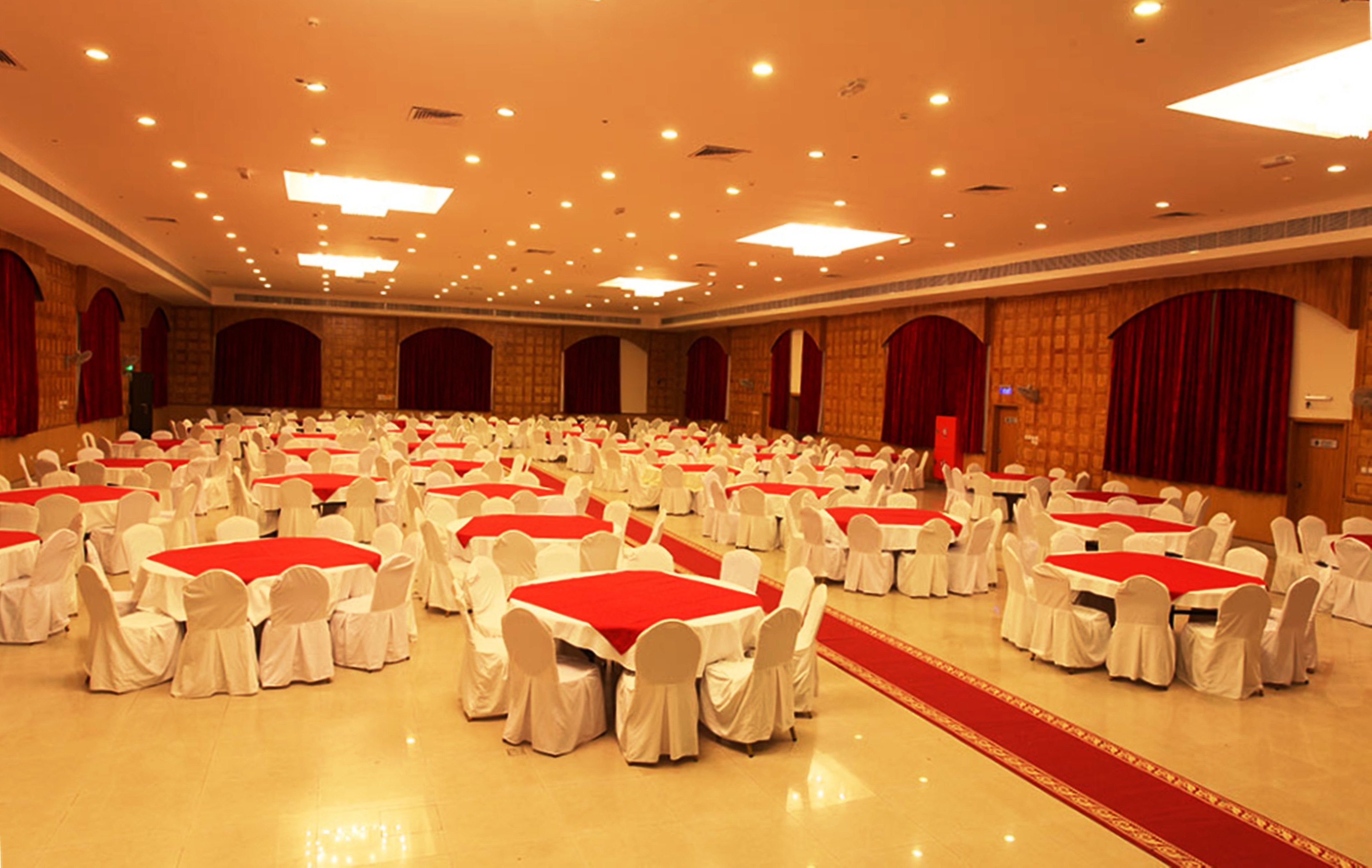 A large banquet hall with multiple round tables covered with red tablecloths and white chairs.