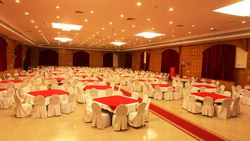 A large banquet hall with multiple round tables covered with red tablecloths and white chairs.