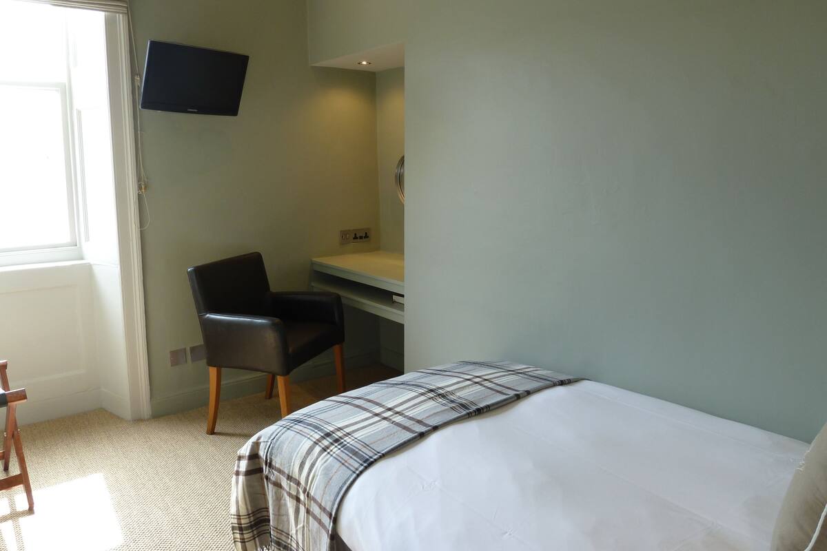 Habitación de hotel con cama, escritorio, silla y televisor montado en la pared.