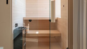 A modern interior with a wooden floor, a glass door leading to a sauna area, and a small sink with a towel. - Baia del Mar Beach Boutique Hotel (Jesolo)