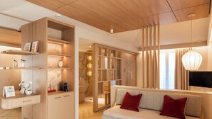 A modern living room with a wooden floor, a beige sofa with red cushions, and built-in wooden shelving. - Baia del Mar Beach Boutique Hotel (Jesolo)