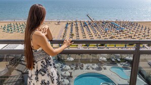 A balcony with a view of a beach with rows of umbrellas and sun loungers, and a pool area. - Baia del Mar Beach Boutique Hotel (Jesolo)