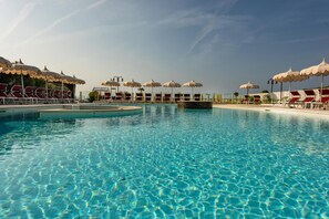 A swimming pool with clear blue water, surrounded by sun umbrellas and lounge chairs. - Baia del Mar Beach Boutique Hotel (Jesolo)