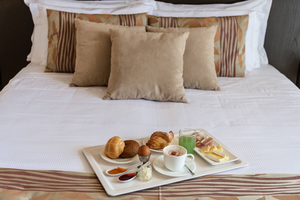 A neatly made bed with a tray of breakfast items including croissants, a cup of coffee, and a glass of juice.