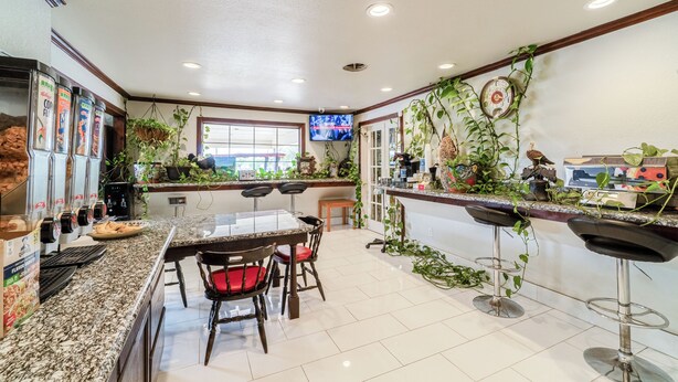 A kitchen with a granite countertop, a dining table with chairs, a coffee machine, and a TV mounted on the wall. - Purple Sage By OYO Snyder TX (Snyder)