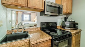 A compact kitchen with wooden cabinets, a stainless steel microwave, a stove, and a sink. - Purple Sage By OYO Snyder TX (Snyder)