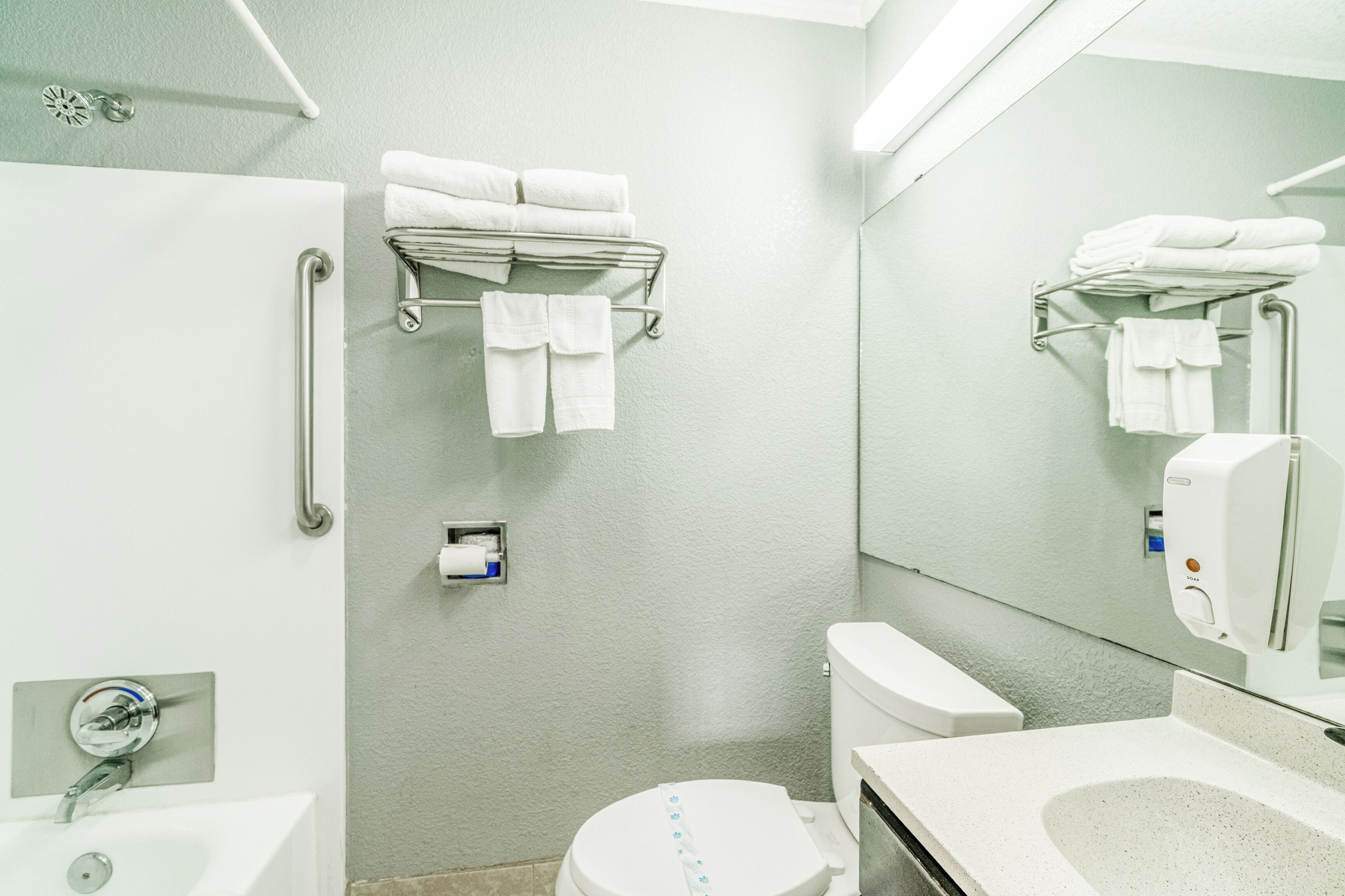 A bathroom with a white sink, toilet, and hand dryer. There are towels on a rack and a mirror above the sink.