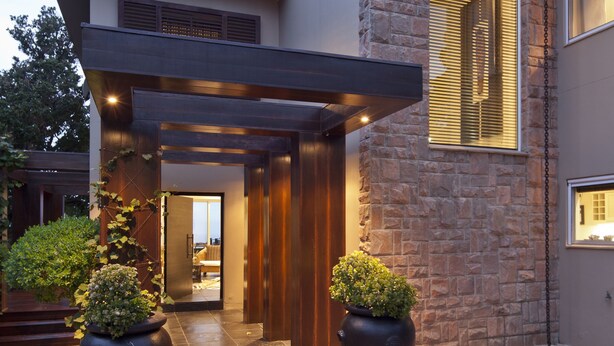 A modern house with a stone facade, a covered entrance, and large potted plants. - Luxury Seaside Homes (Pennington)