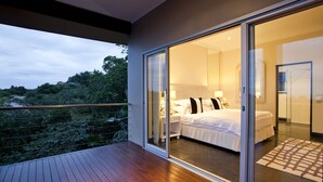 A bedroom with a large sliding glass door leading to a balcony. The room has a bed with white bedding and a nightstand with a lamp. - Luxury Seaside Homes (Pennington)