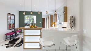 A modern kitchen with a central island, pendant lighting, and a dining area with white chairs. - Luxury Seaside Homes (Pennington)