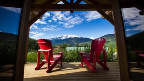 A wooden deck with two red Adirondack chairs facing a mountain view. - Heather Mountain Lodge (Golden)