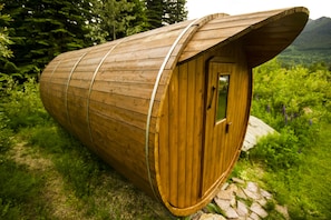 A wooden cabin with a curved roof, situated on a stone path surrounded by greenery. - Heather Mountain Lodge (Golden)