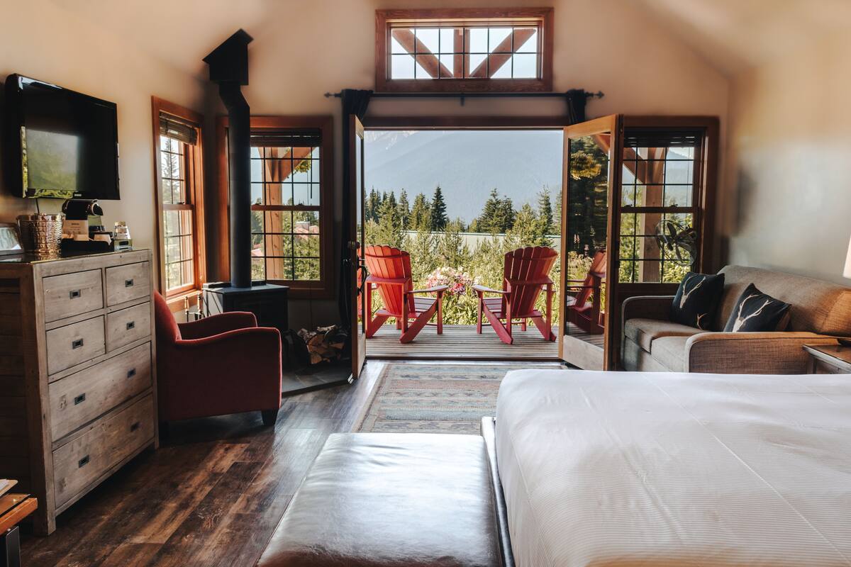 A bedroom with a large bed, a dresser, a TV, and a view of a patio with chairs and a table.