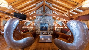A rustic interior with a stone fireplace, wooden beams, and leather armchairs. - Heather Mountain Lodge (Golden)