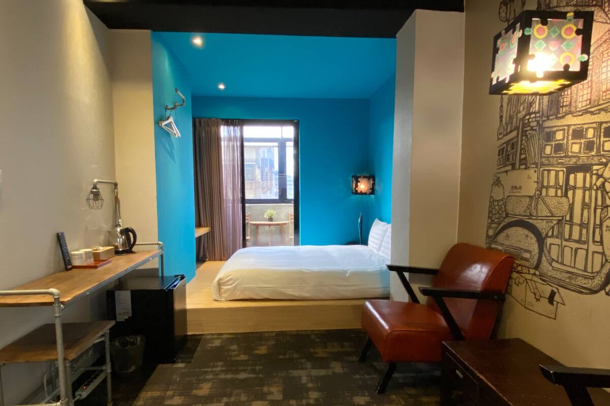 Une chambre d’hôtel avec un lit, un bureau, une chaise et un mur orné d’une fresque représentant un paysage urbain.
