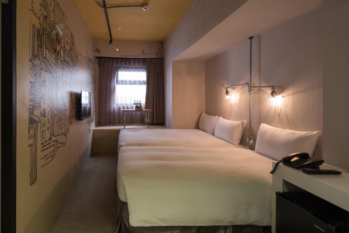 Une chambre d’hôtel avec deux lits, un bureau avec un téléphone et un téléviseur fixé au mur.
