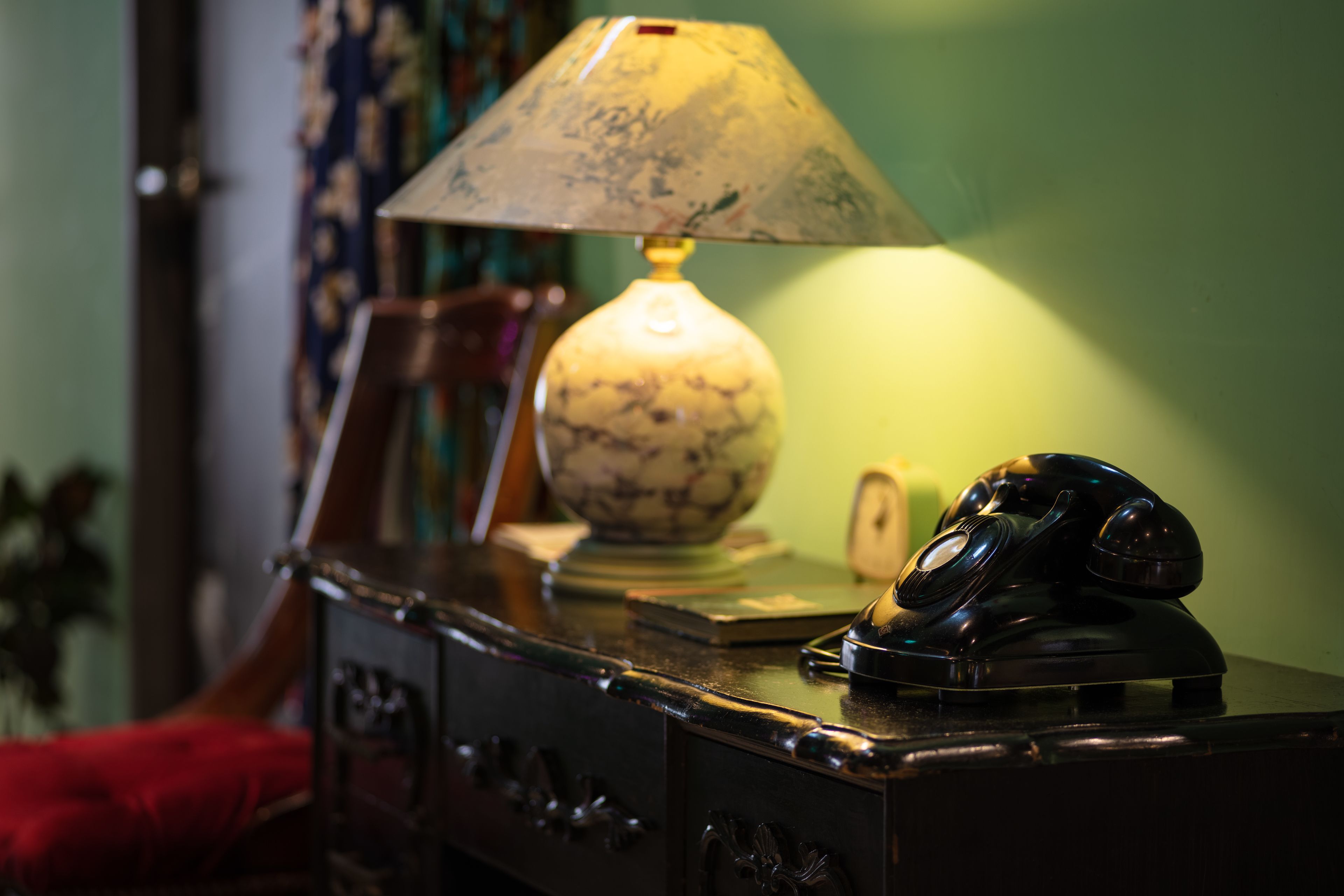A desk with a lamp, a rotary phone, and a bowl.