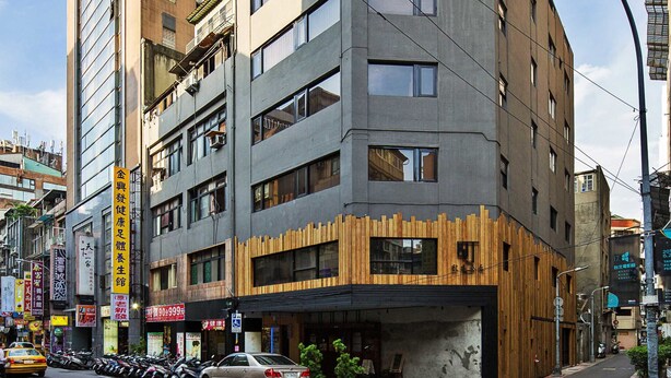 A multi-story building with a modern architectural design, featuring a mix of concrete and wooden elements, and a visible entrance with a ramp. - Cho Hotel (Taipei)