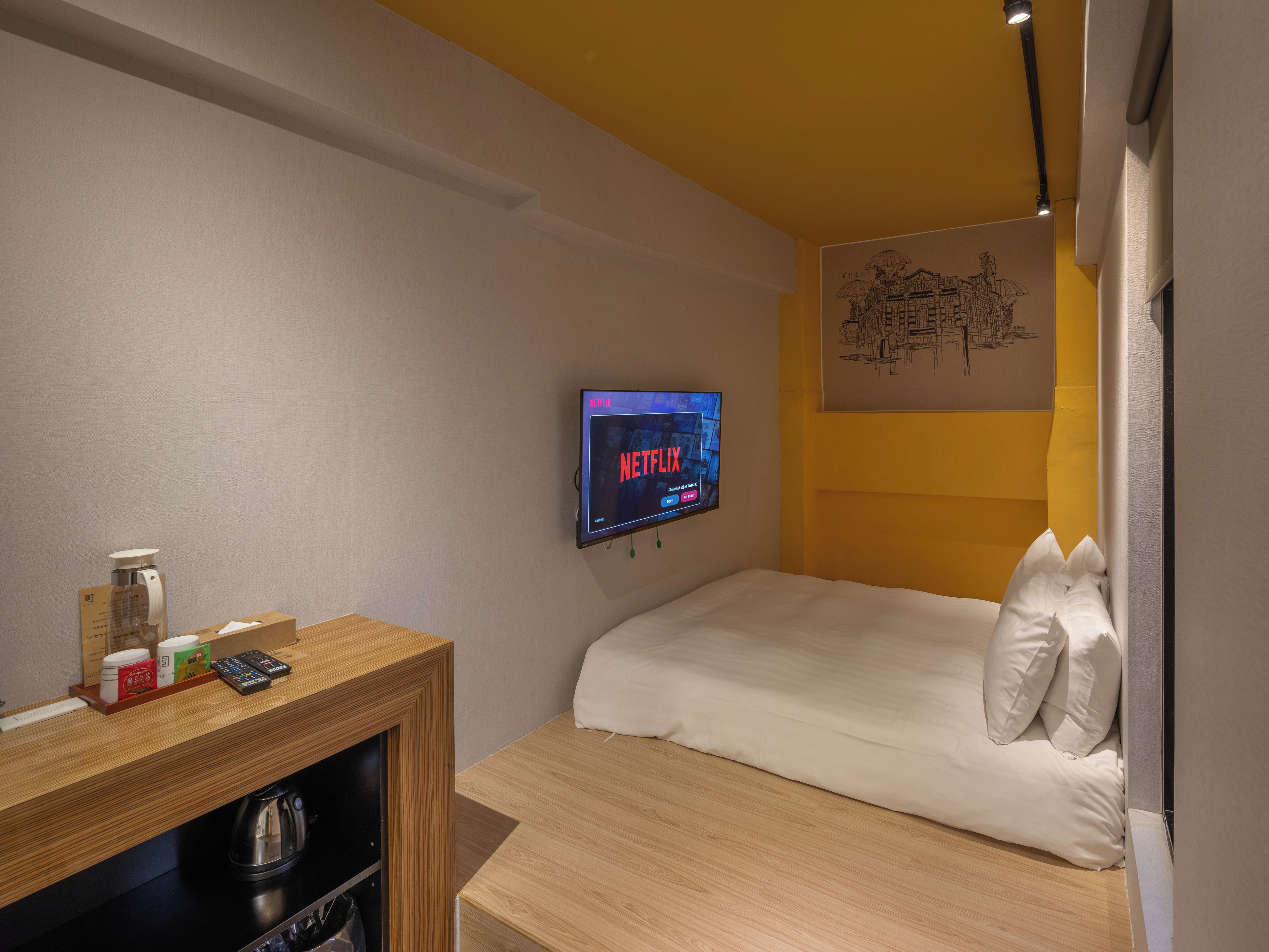 Une chambre d’hôtel avec un lit, un bureau doté d’une bouilloire, une télécommande et un téléviseur fixé au mur affichant le logo de Netflix.