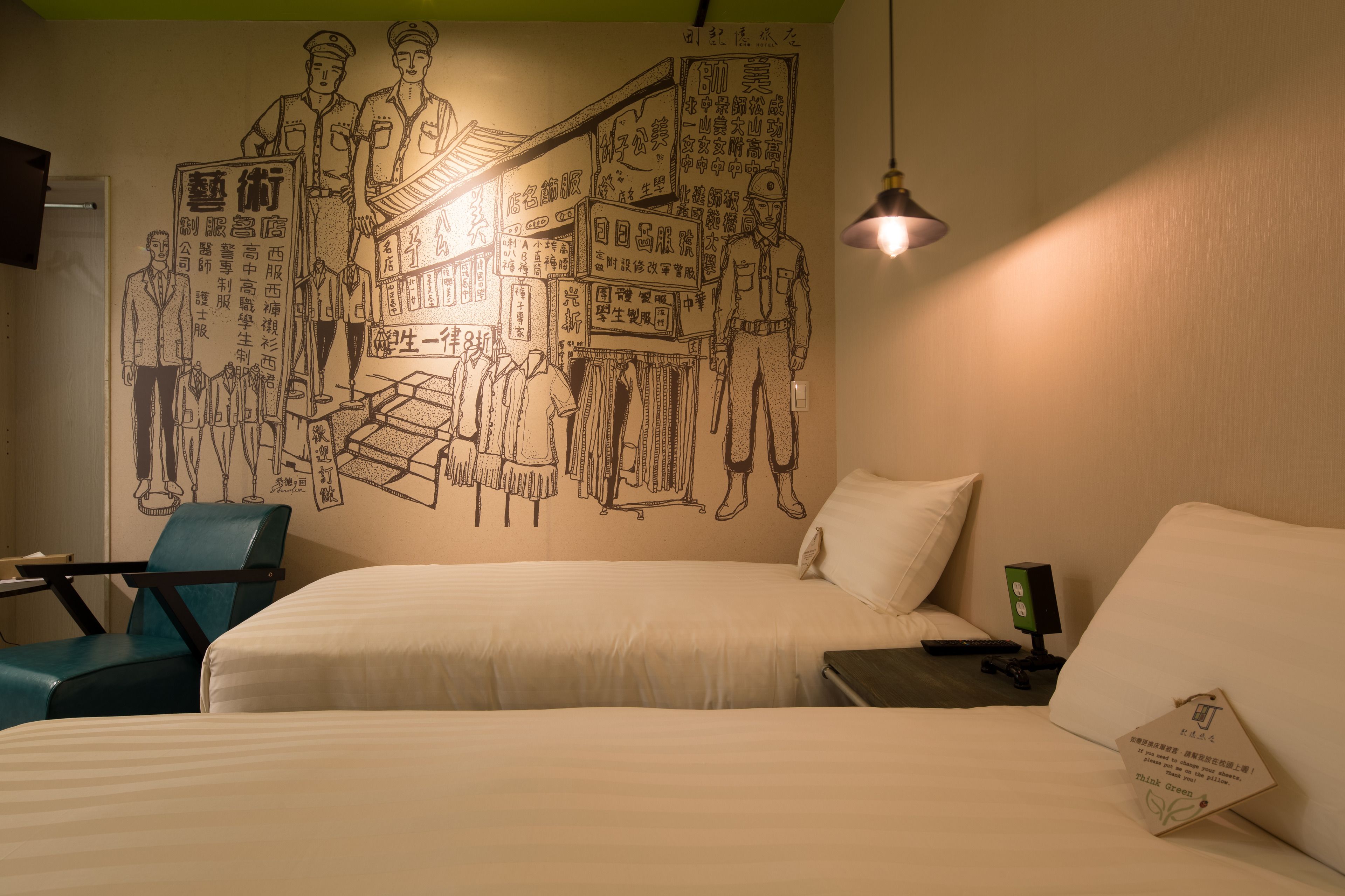 Een hotelkamer met twee bedden, een bureau en een stoel. Op de muur bevindt zich een muurschildering met diverse figuren en tekst.