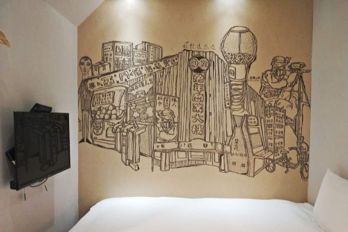 Une chambre d’hôtel avec une grande fresque murale représentant un paysage urbain avec différents bâtiments et un distributeur automatique.