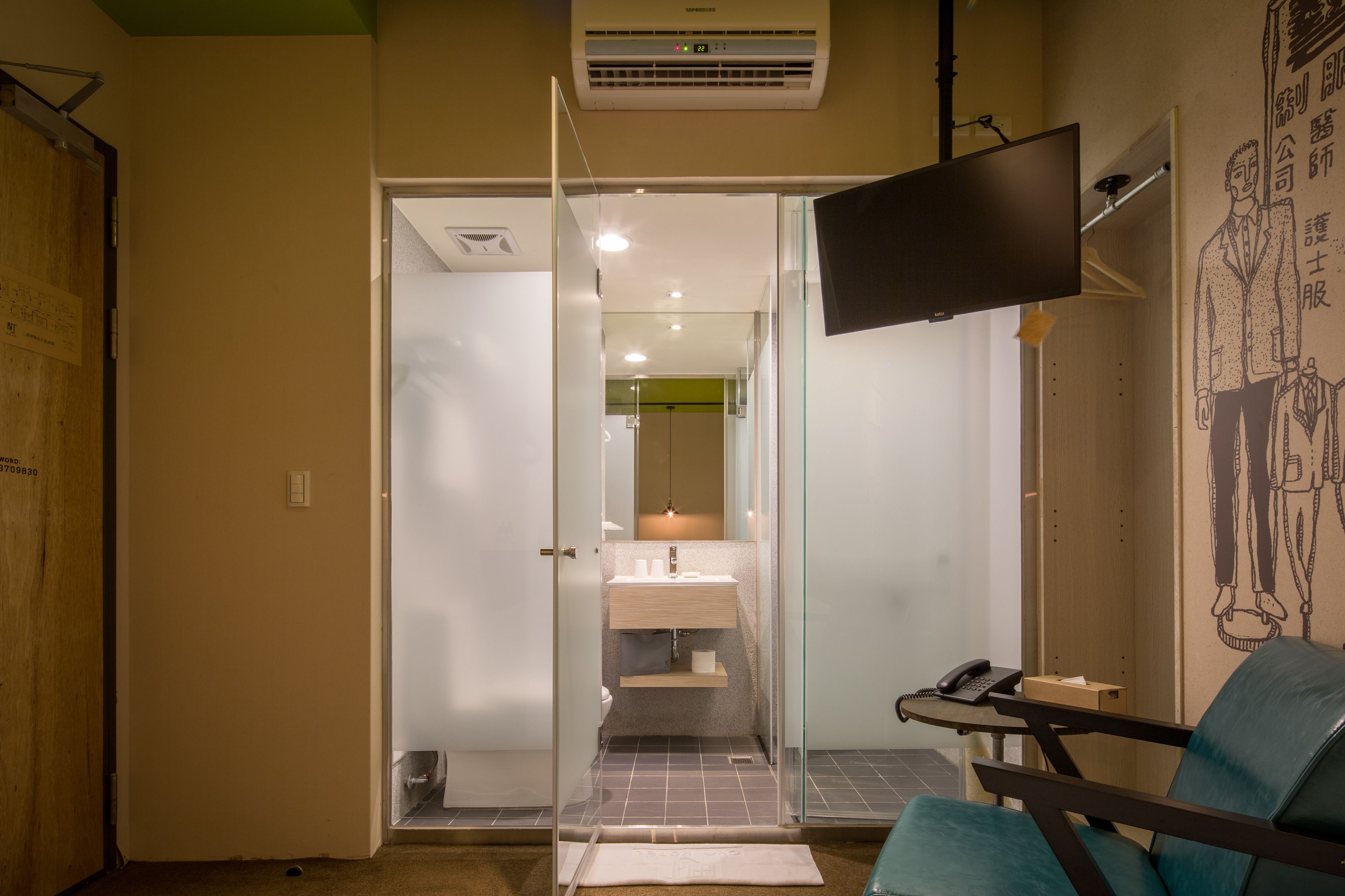Habitación de hotel con puerta de vidrio que da al baño, televisor de pantalla plana montado en la pared y una silla en la esquina.