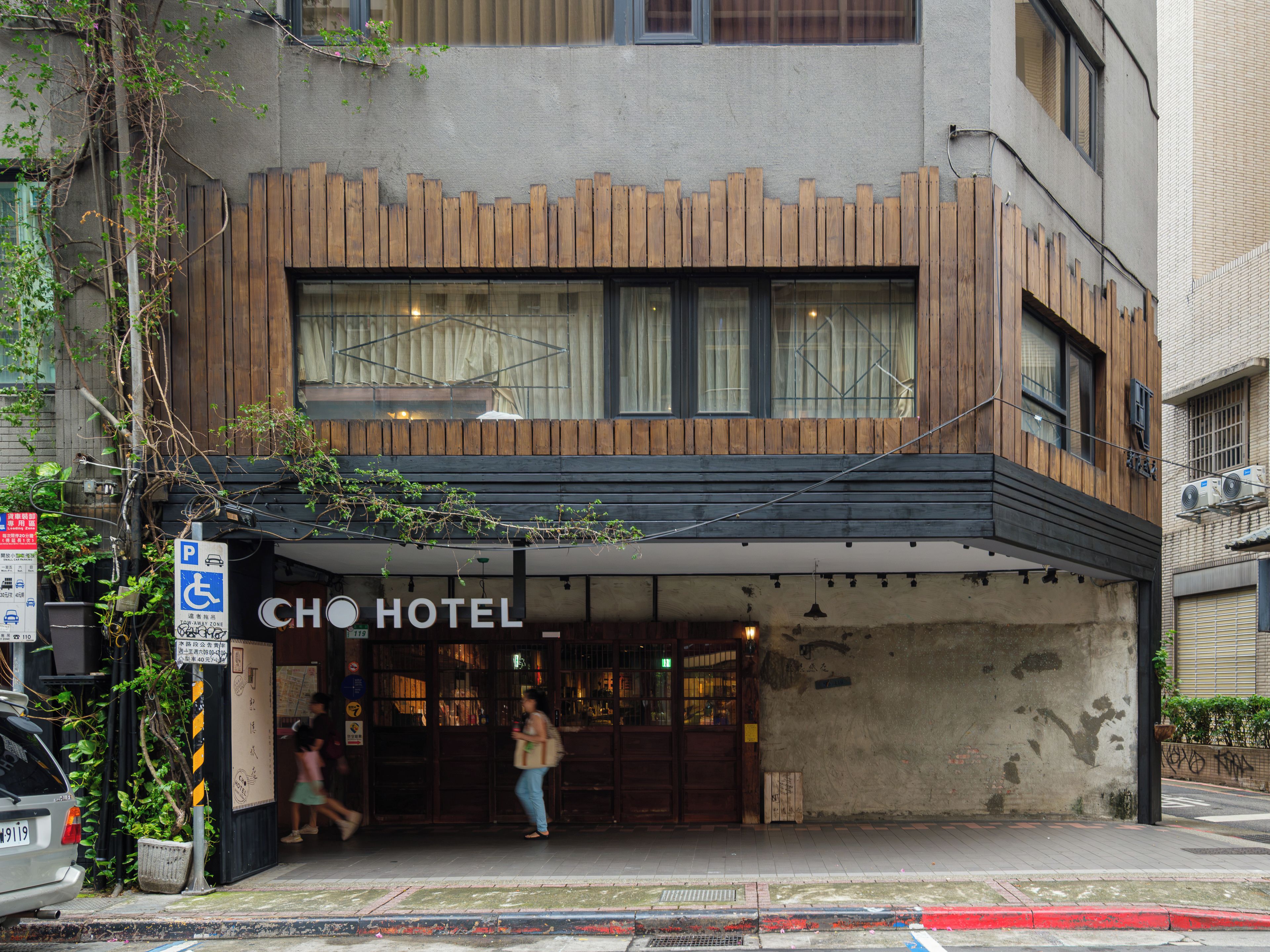 A hotel entrance with a wooden facade, a signboard, and a disabled parking sign.