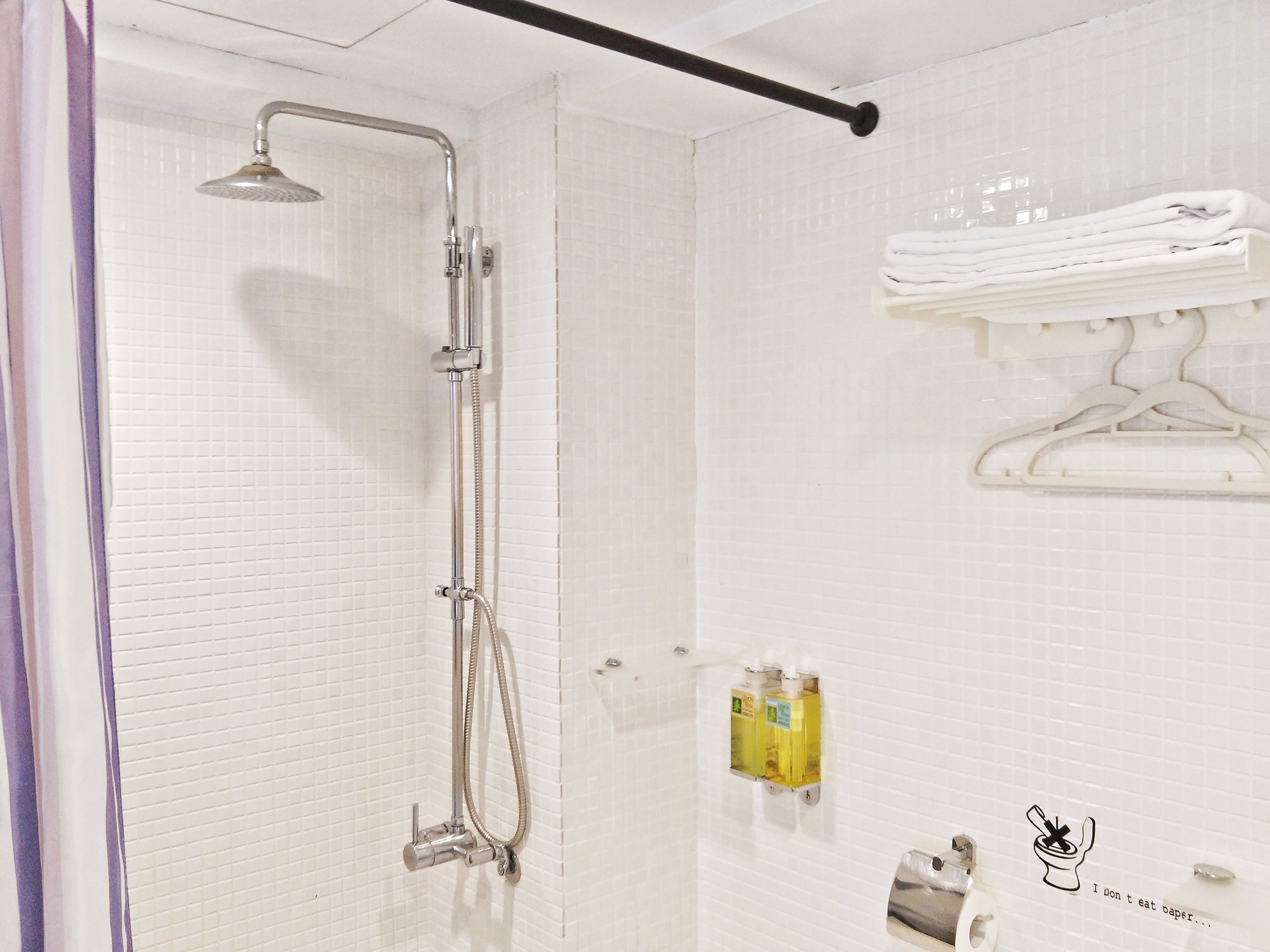 A shower with a handheld showerhead, a wall-mounted towel rack with folded towels, and a soap dispenser on the wall.
