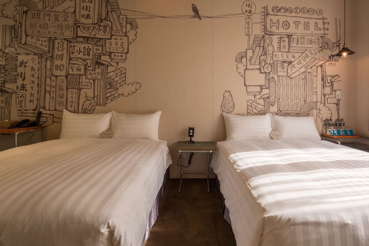 Une chambre d’hôtel avec deux lits, une petite table et un mur décoré d’une fresque représentant un paysage urbain.