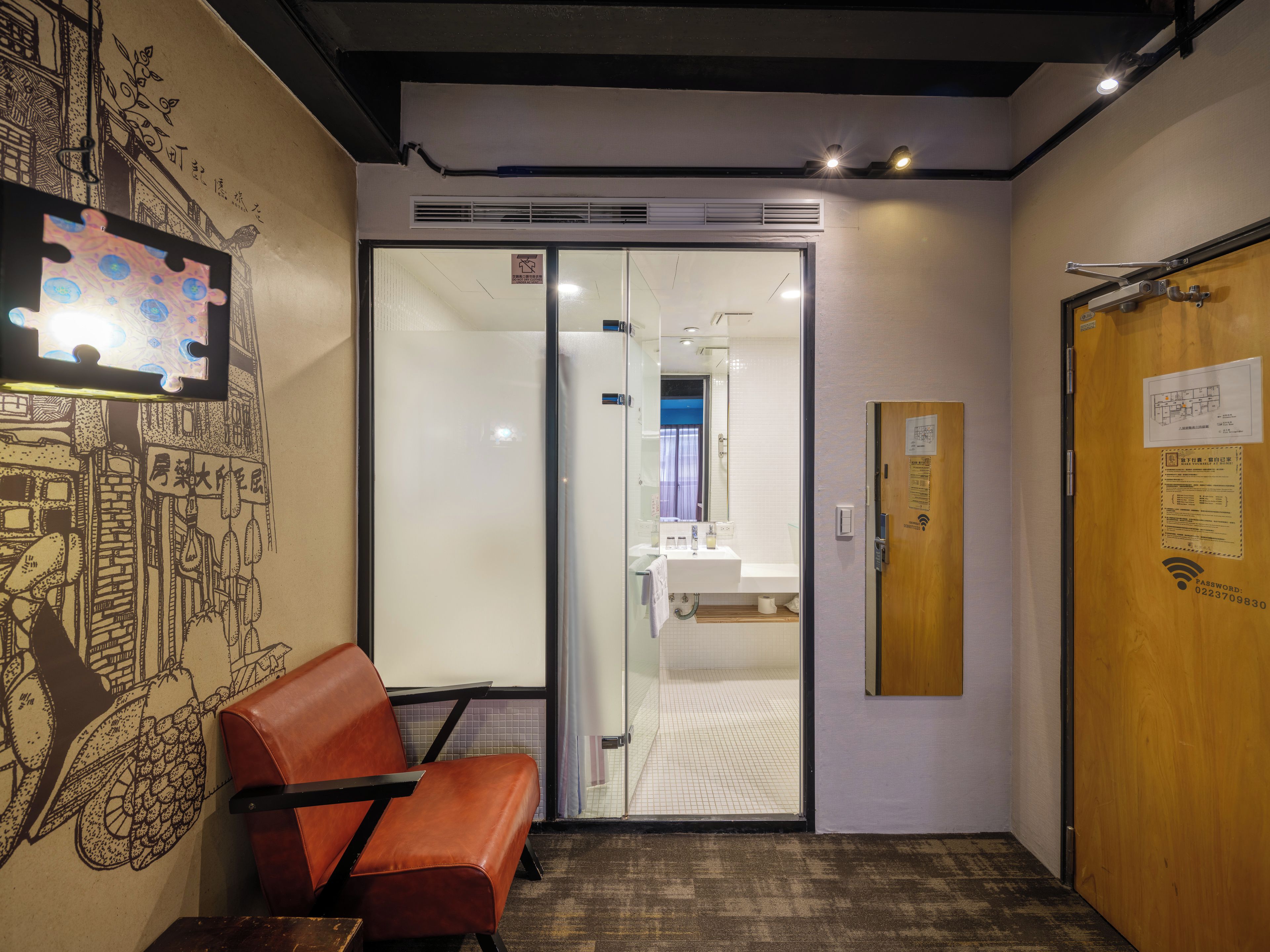 A hotel corridor with a glass door leading to a bathroom, a wooden door with a sign, and a wall with a decorative mural.
