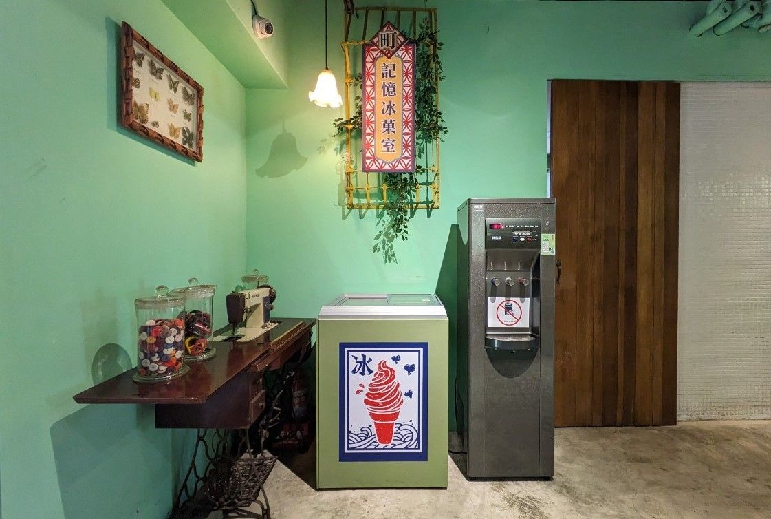 A room with a green wall, a wooden door, a vending machine, and a table with jars of candies.