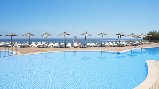 Ein Schwimmbecken mit Liegestühlen und Sonnenschirmen, ein klarer Himmel und Blick aufs Meer.