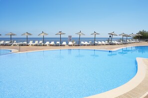 Une piscine avec des chaises longues et des parasols, un ciel dégagé et une vue sur la mer.