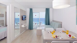 Ein modernes Hotelzimmer mit Balkon, einer Essecke mit Frühstück und einem an der Wand befestigten Fernseher.