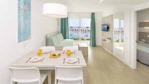 Ein modernes Hotelzimmer mit Essbereich, einem Bett mit Blick auf den Pool und einem an der Wand befestigten Fernseher.