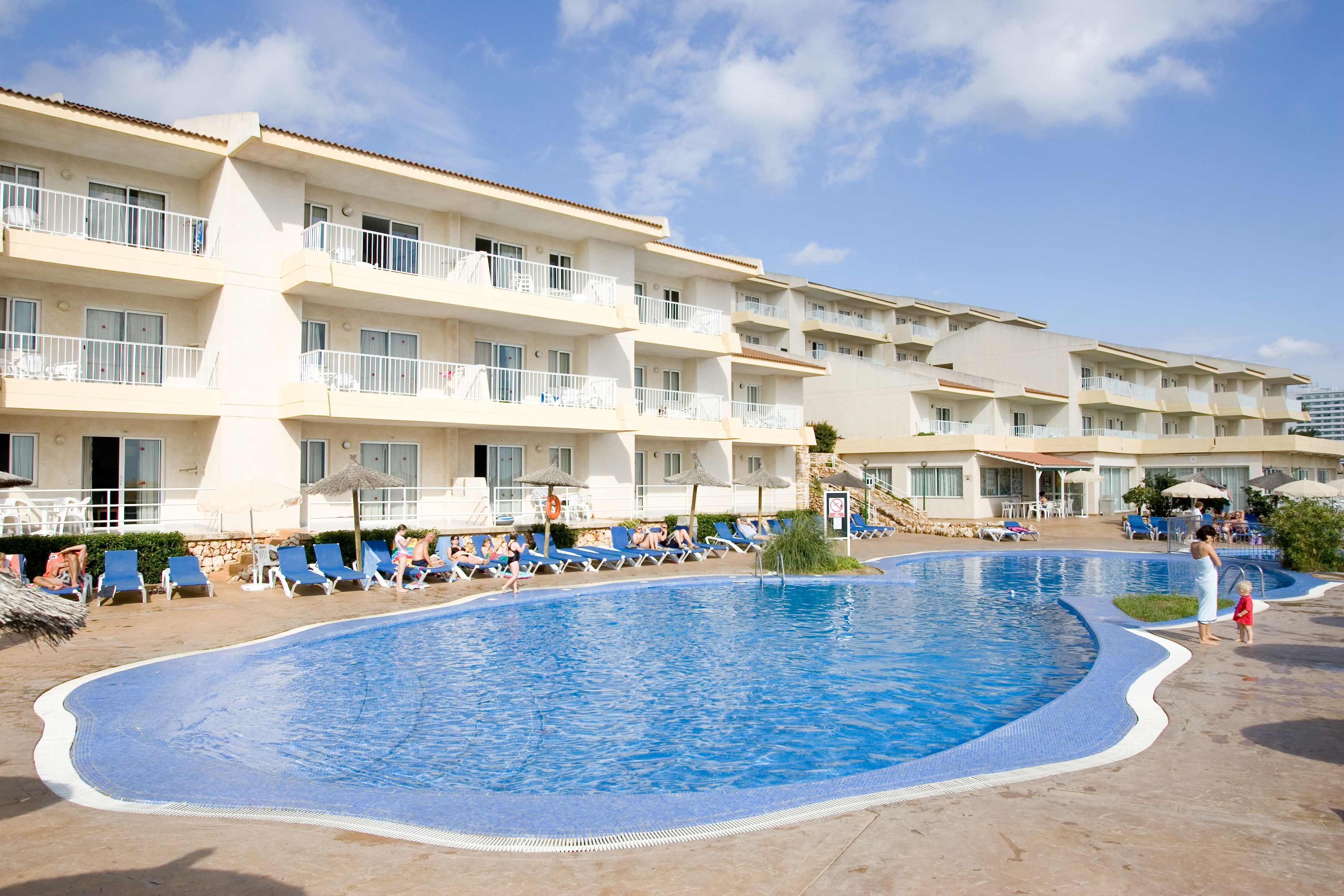 A hotel with a large swimming pool, multiple balconies, and sun loungers.
