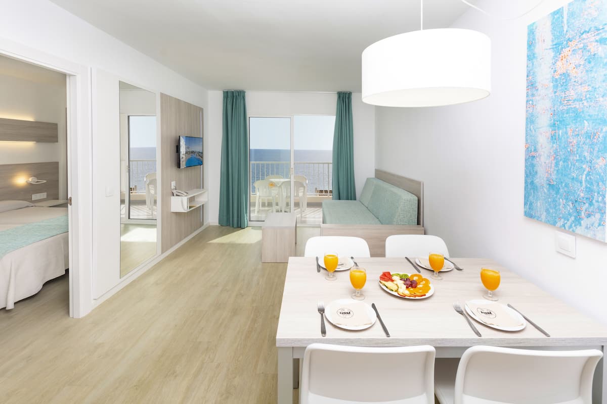 Une chambre d’hôtel moderne dotée d’un coin repas, d’un balcon avec vue sur la mer et d’un grand tableau abstrait accroché au mur.