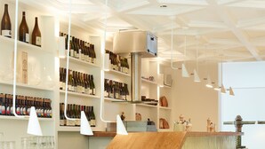 A modern bar area with wooden counters, shelves of wine bottles, and hanging pendant lights. - Hotel des Galeries (Brussels)