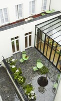 A courtyard with a glass enclosure, green chairs, and potted plants.