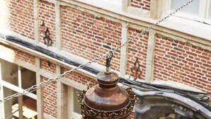 A vintage street lamp with a chain, a brick building with large windows, and a white fence. - Hotel des Galeries (Brussels)
