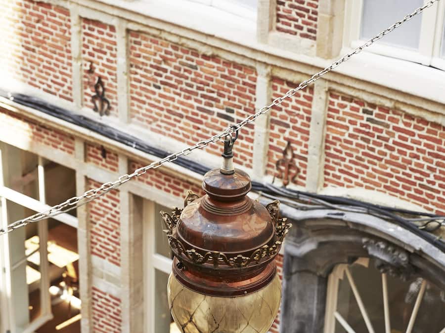 A vintage street lamp with a chain, a brick building with large windows, and a white fence.
