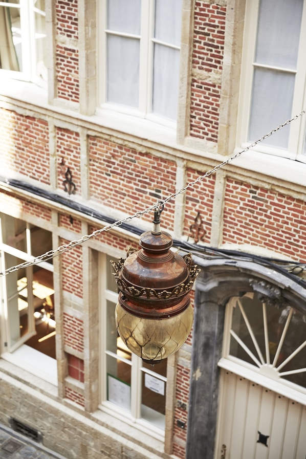 A vintage street lamp with a chain, a brick building with large windows, and a white fence. - Hotel des Galeries (Brussels)