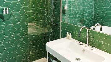 Un baño moderno con ducha de vidrio, un lavabo blanco y baldosas hexagonales verdes.