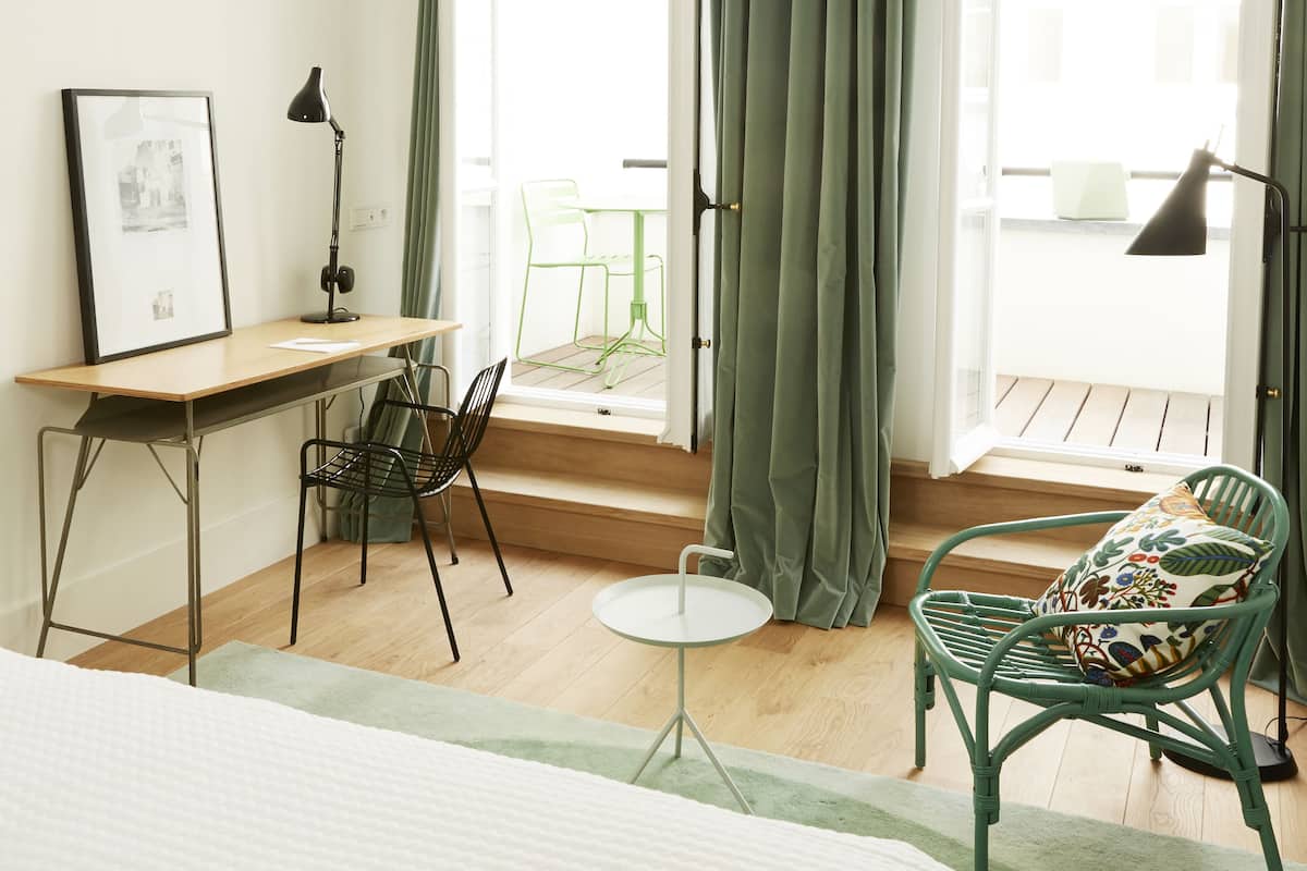 Hotellihuone, jossa on sänky, työpöytä, tuoli ja parveke, jossa on verhot.
