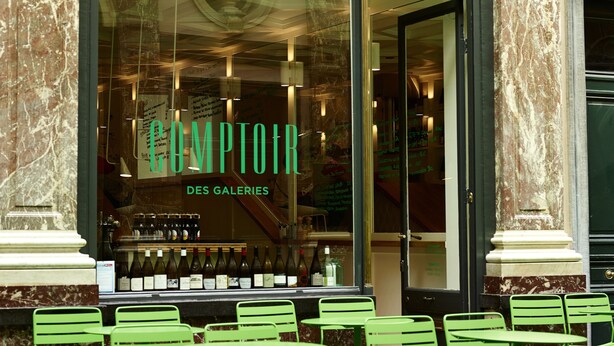 A building with a large arched window, a sign reading "COMPTOIR DES GALLERIES", and green metal chairs outside. - Hotel des Galeries (Brussels)