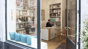 A hotel reception area with a receptionist, a reception desk, and a bookshelf filled with books. - Hotel des Galeries (Brussels)