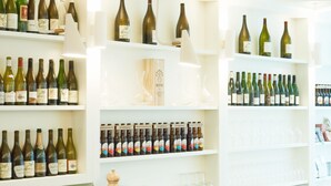 A bar area with shelves of wine bottles, a wooden counter, and two white bar stools. - Hotel des Galeries (Brussels)