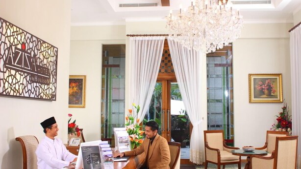 A hotel reception area with a reception desk, a chandelier, and a seating area with chairs and a table.